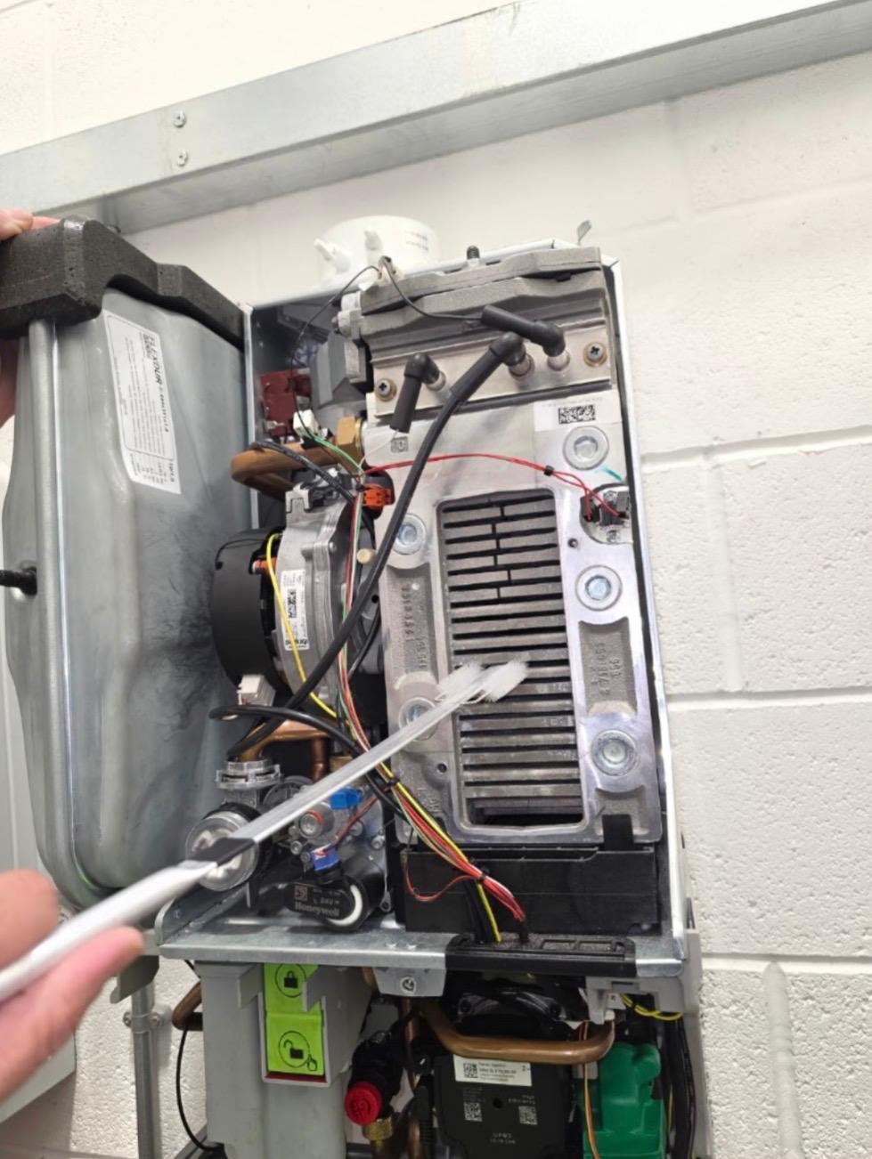 Combi boiler opened up for service showing heat exchanger, fan and ignition leads